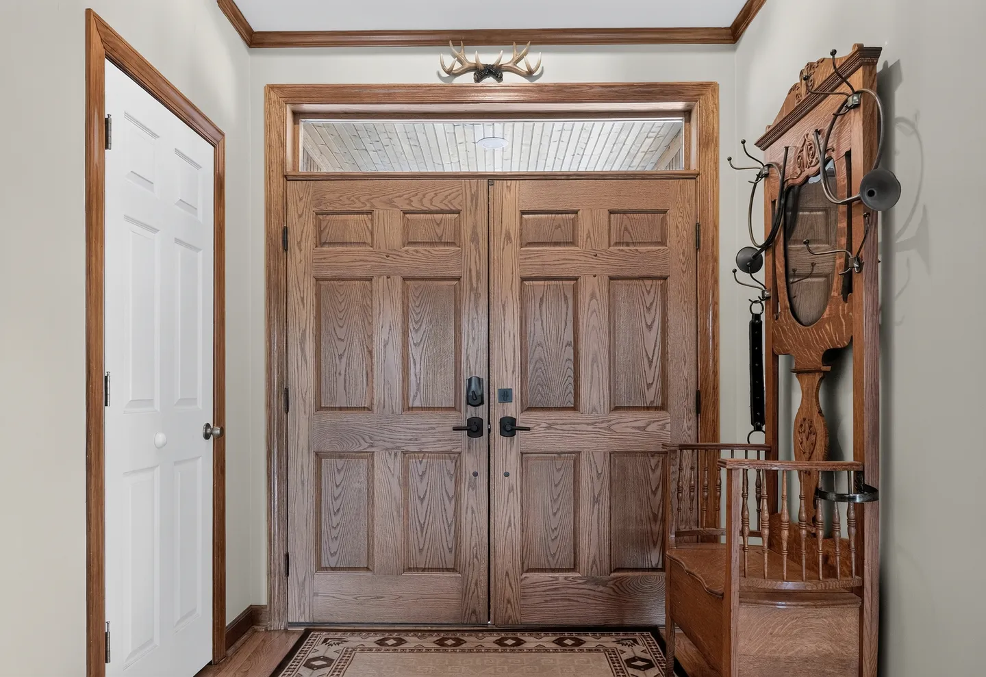 Front entrance interior featuring double wooden paneled doors with a transom window above and an antique hall tree to the right.