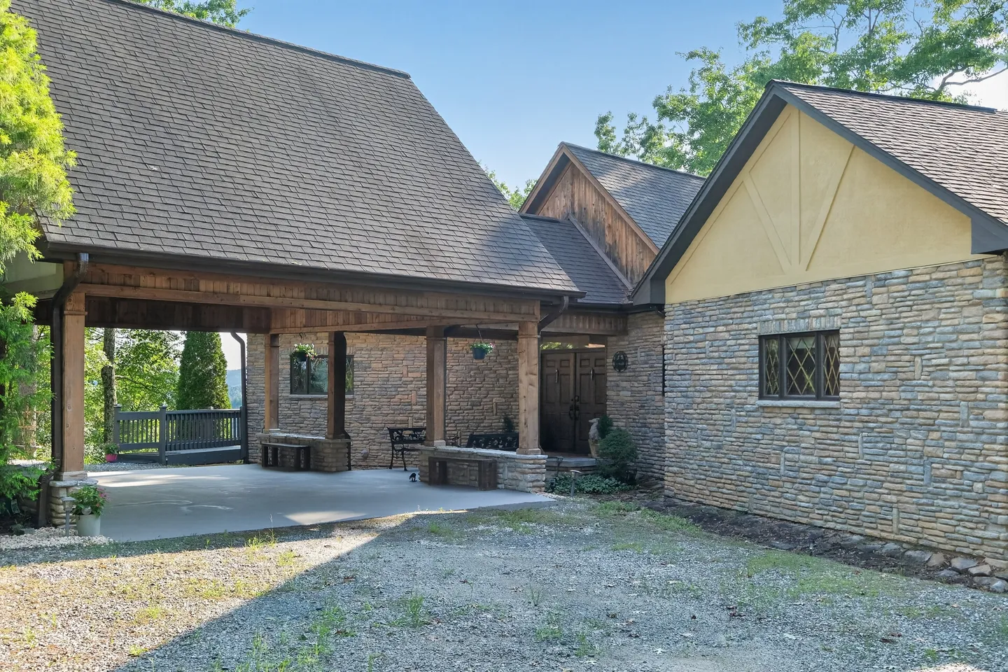 Exterior of a stone and timber home showing a gravel driveway, covered carport entrance, and double front doors.