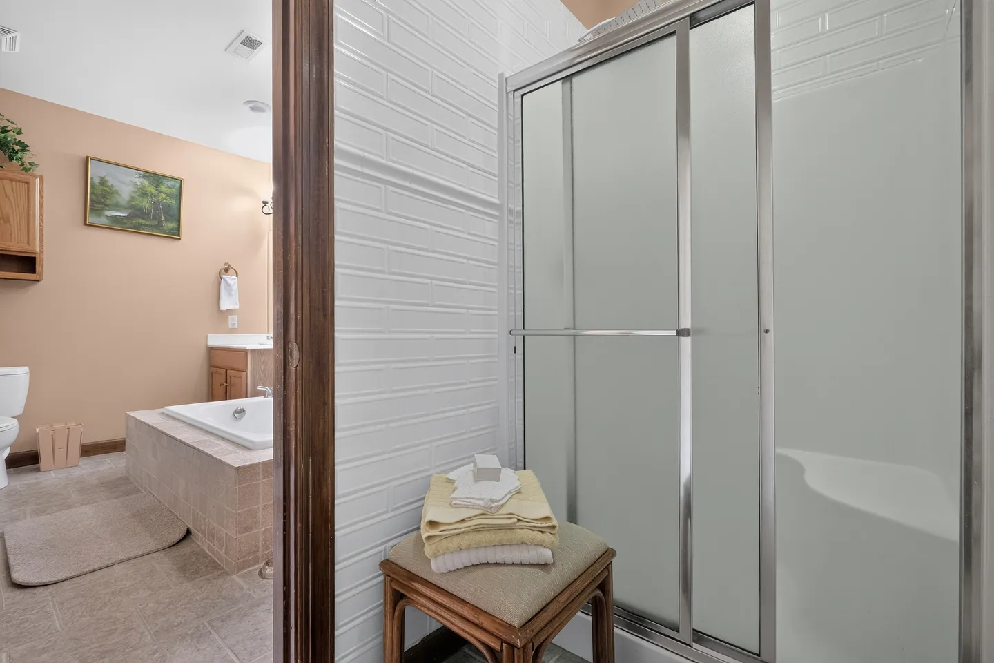 Bathroom with white tiled wall, sliding glass shower door, and a glimpse into an adjoining area with a soaking tub and vanity.