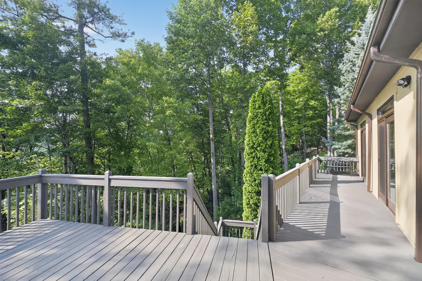 Outdoor elevated deck with gray railings and plank flooring overlooking lush green trees.