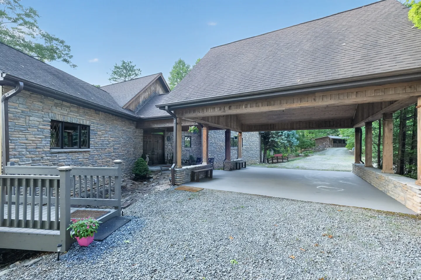 Stone and wood exterior of a home featuring a large covered carport attached to the house with a gravel driveway.