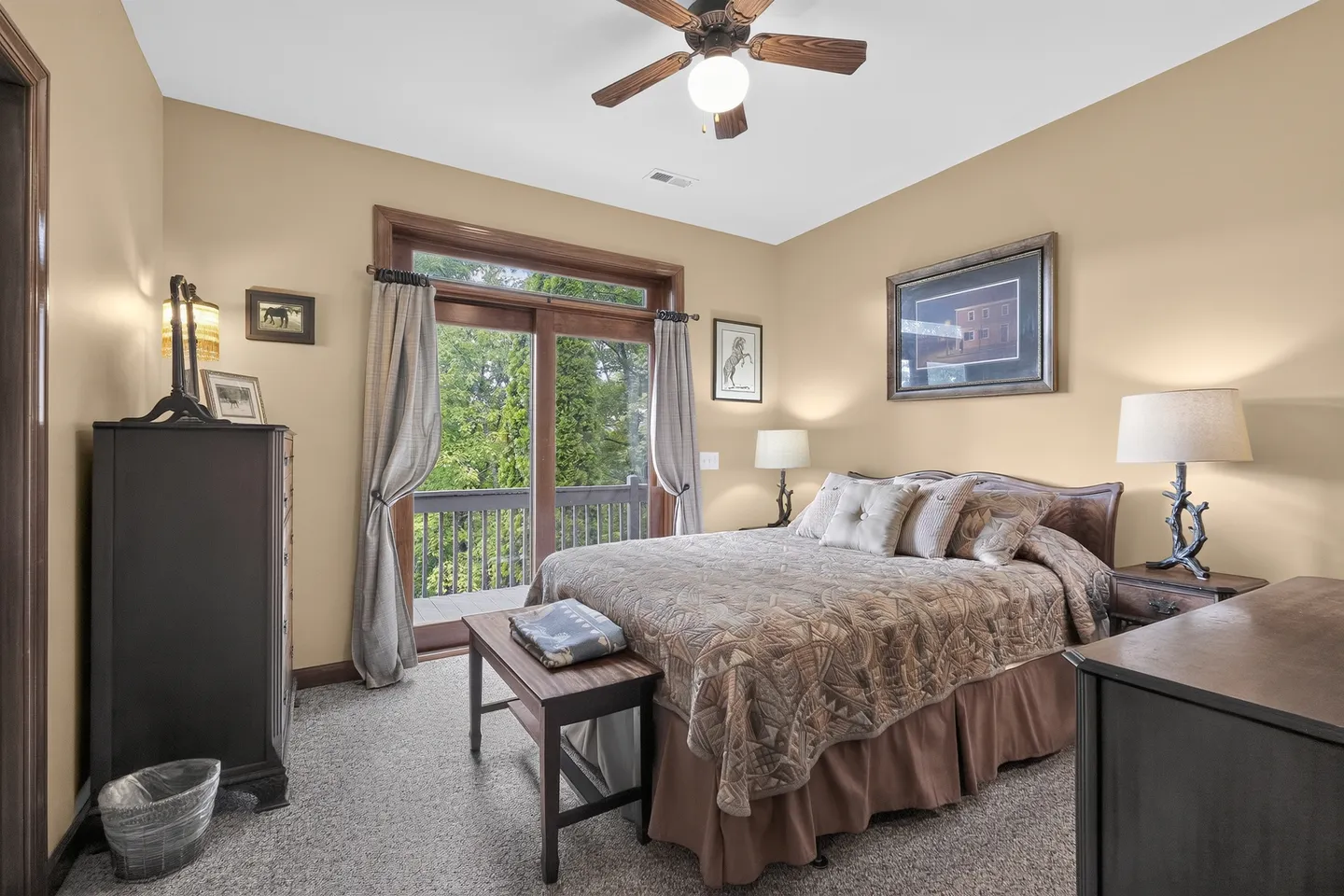 Bedroom featuring a made bed, carpeted floors, dresser, nightstands with lamps, ceiling fan, and sliding glass doors opening to an outdoor deck.