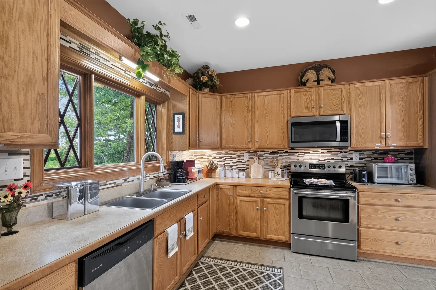 Kitchen with light wood cabinetry, laminate countertops, a double sink under a large window, and stainless steel appliances.