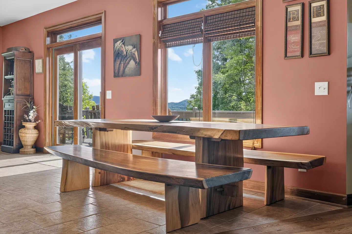 Dining area with a live-edge wooden table and matching benches next to large windows and glass doors.