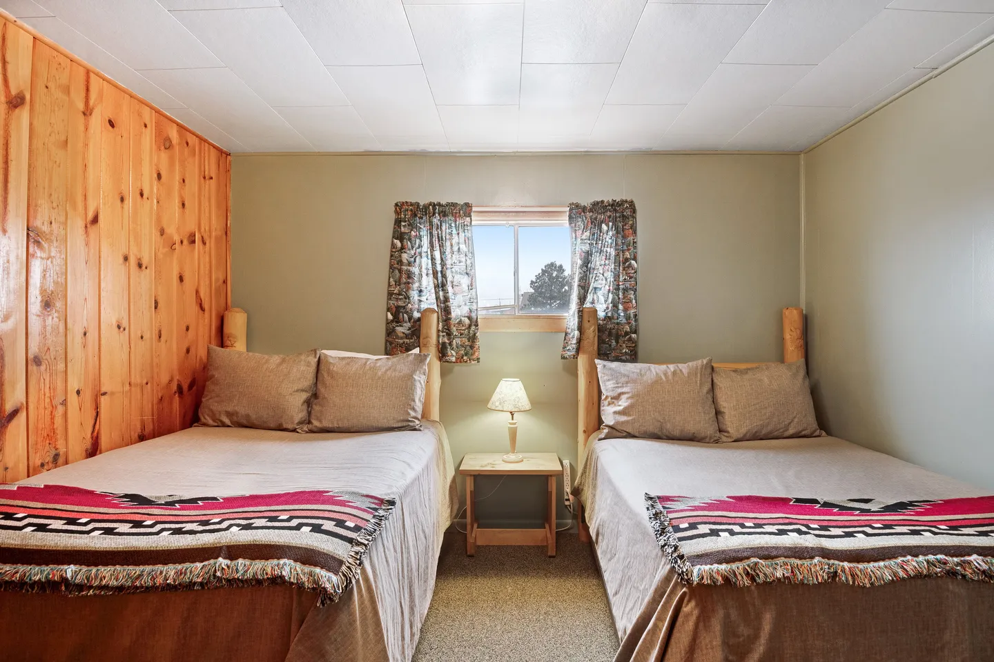 Bedroom featuring two beds with wooden log headboards and Southwestern-patterned throw blankets separated by a small nightstand with a lamp.