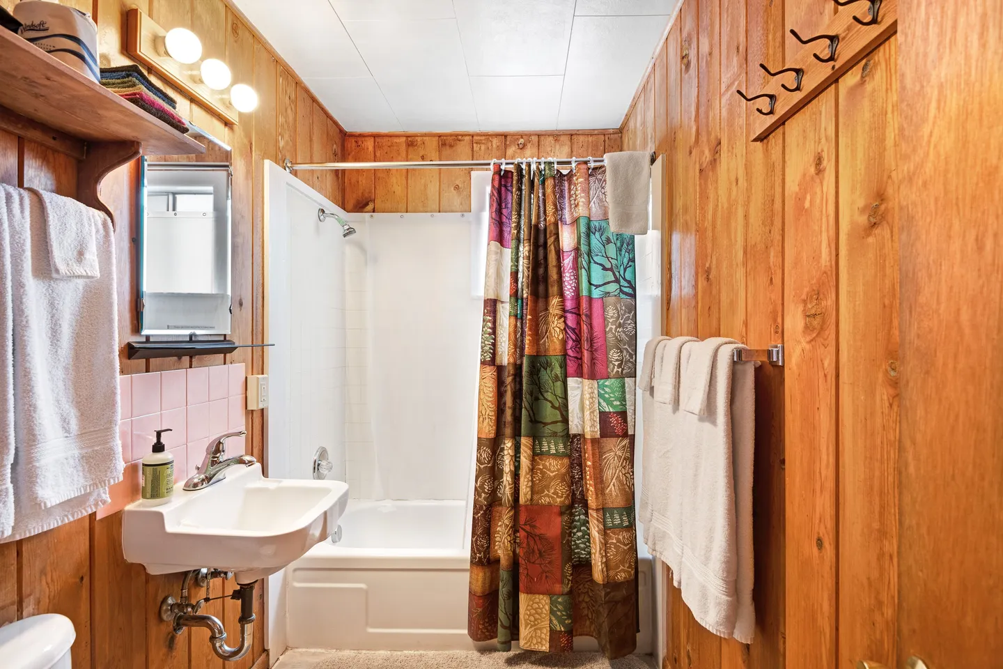 Bathroom with wood-paneled walls, a wall-mounted sink, and a combination bathtub and shower with a colorful patchwork shower curtain.