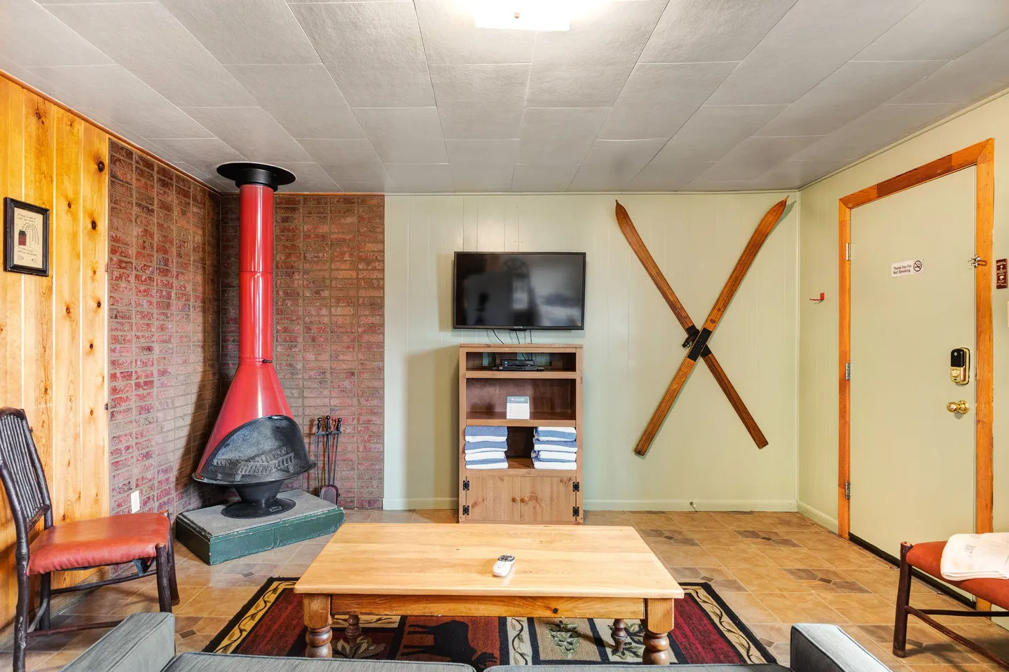 A living room area with a retro freestanding red fireplace, a wall-mounted TV, decorative crossed wooden skis, and a coffee table.
