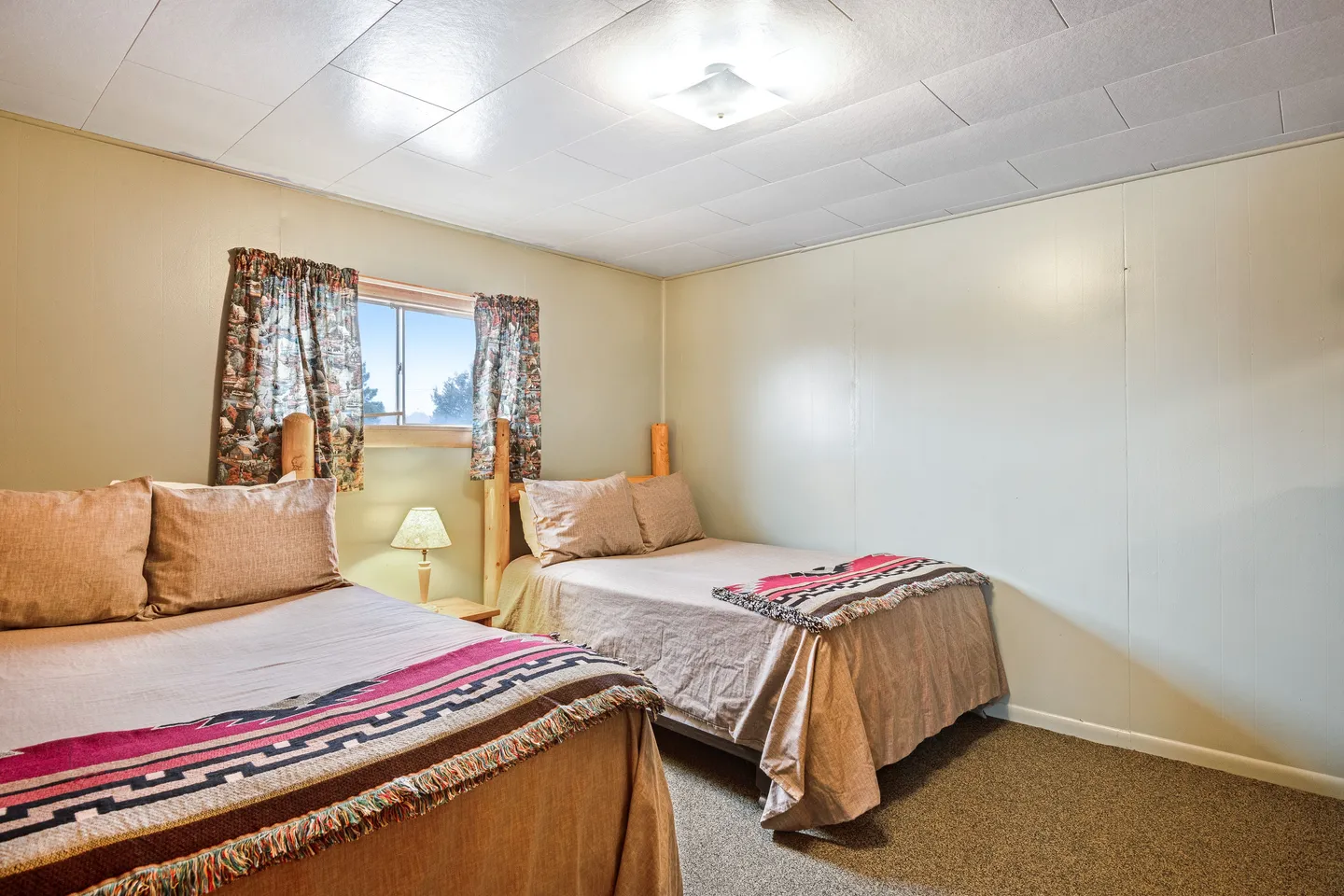 Bedroom with two beds featuring log-style headboards, patterned throw blankets, and a small window with patterned curtains.