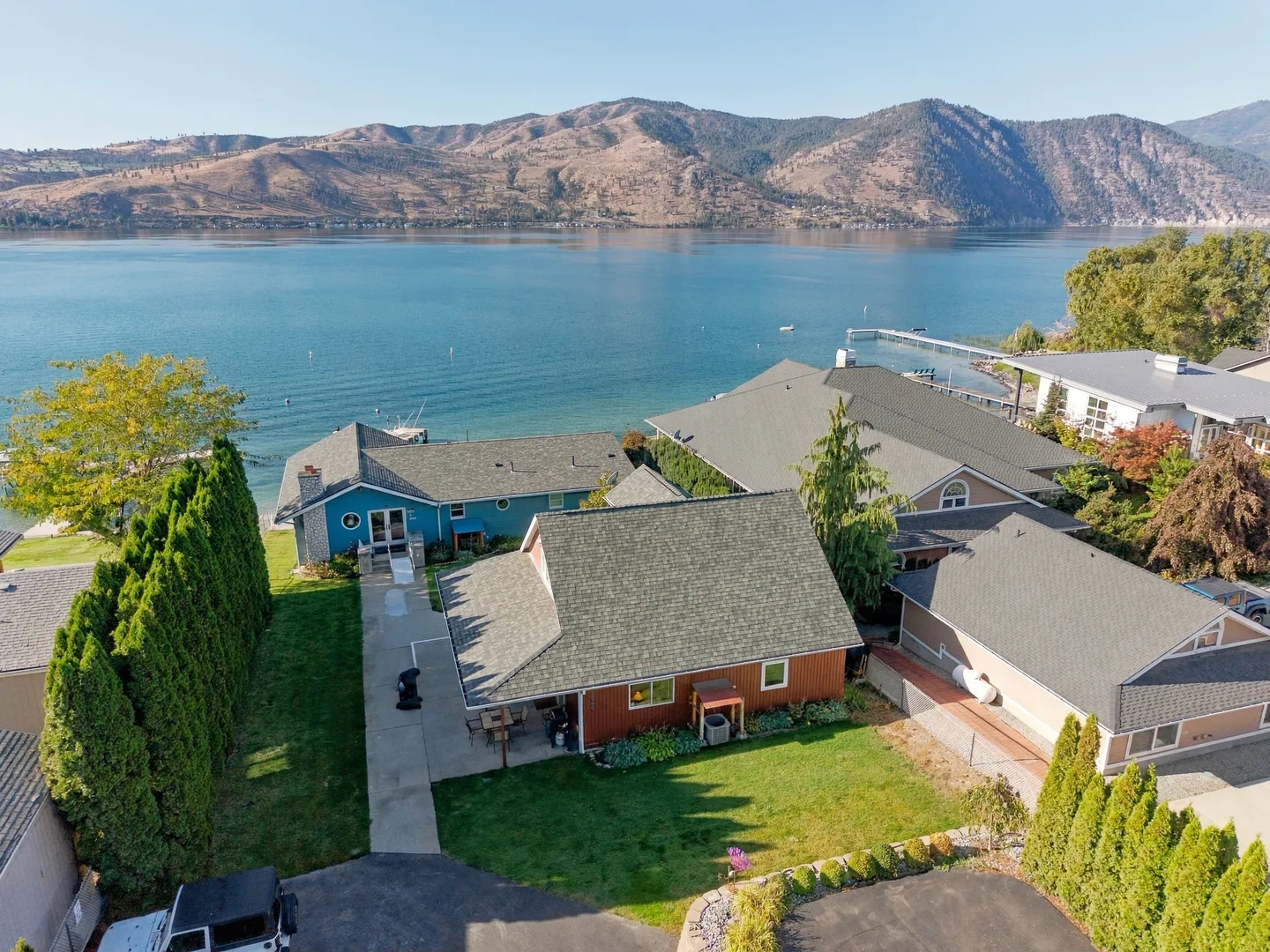 Aerial view of waterfront houses nestled along a wide blue lake with arid mountains in the background under clear skies.
