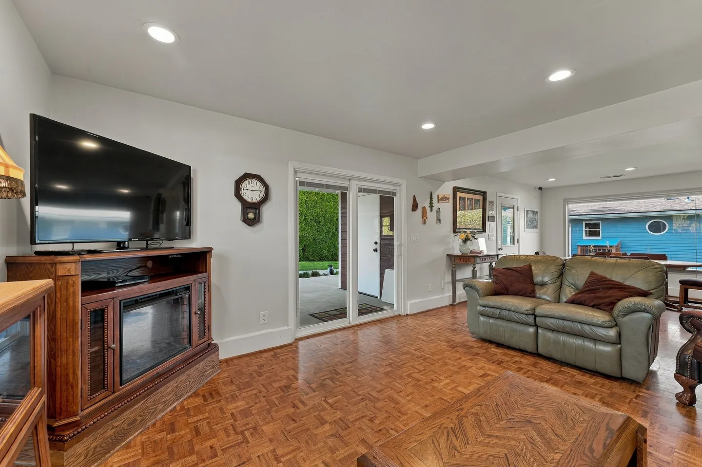 Living room with patterned wood-look flooring, a TV console with built-in electric fireplace, leather sofa, and sliding glass doors leading to a patio.