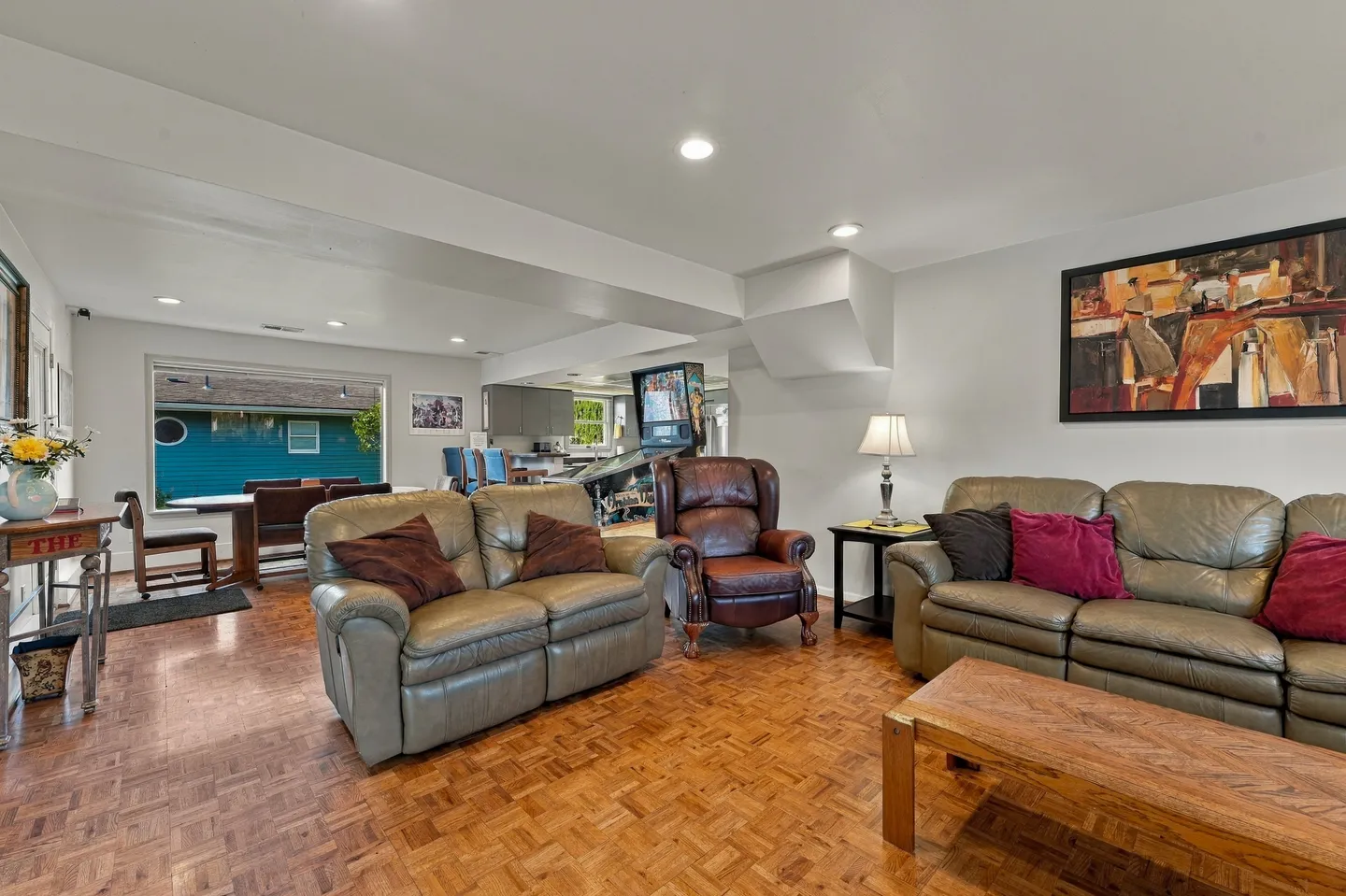 Open living area with parquet wood floors, leather seating, a dining space, and a pinball machine in the background.