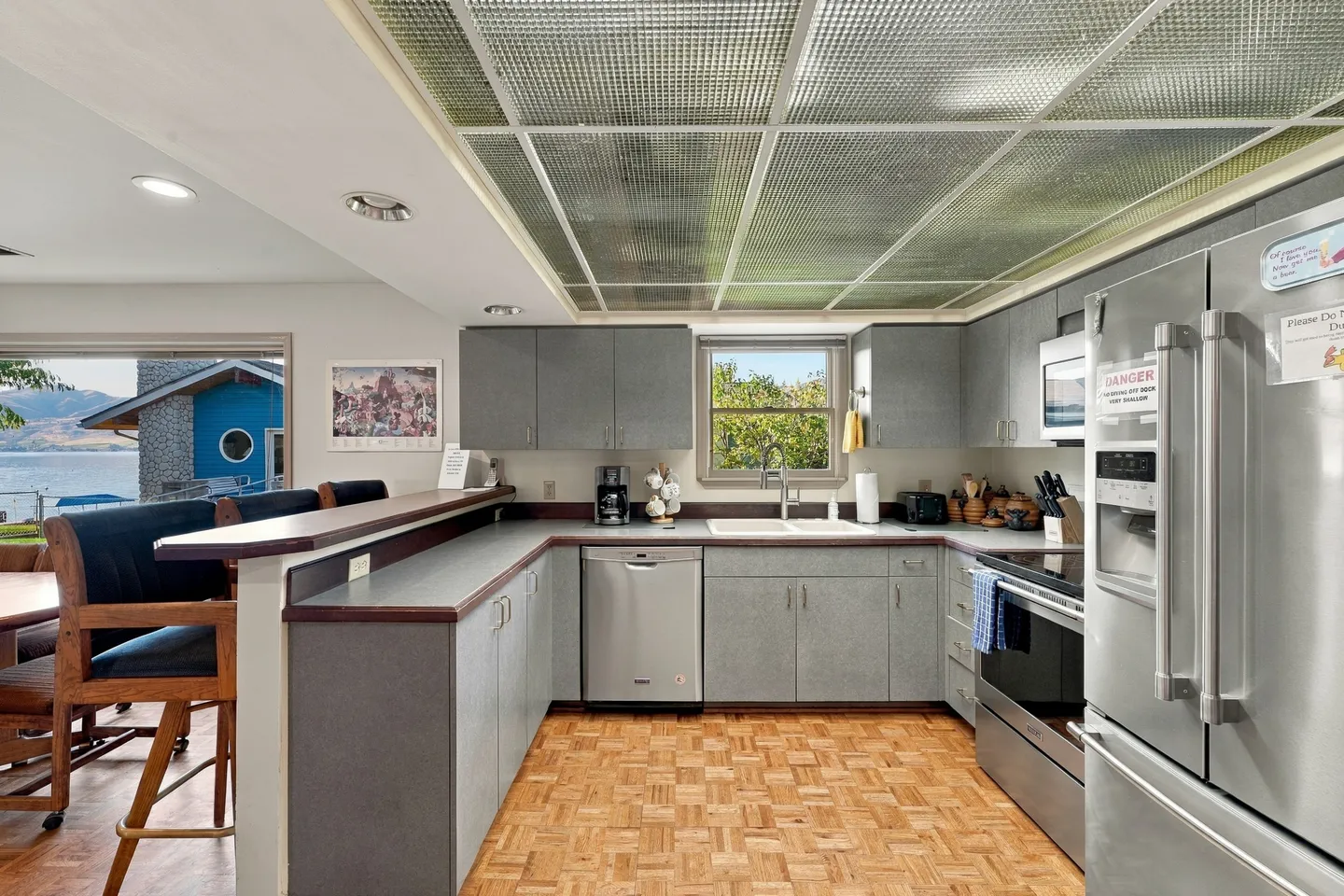 Kitchen with gray cabinetry, stainless steel appliances, a breakfast bar with tall chairs, parquet flooring, and a luminous drop ceiling.