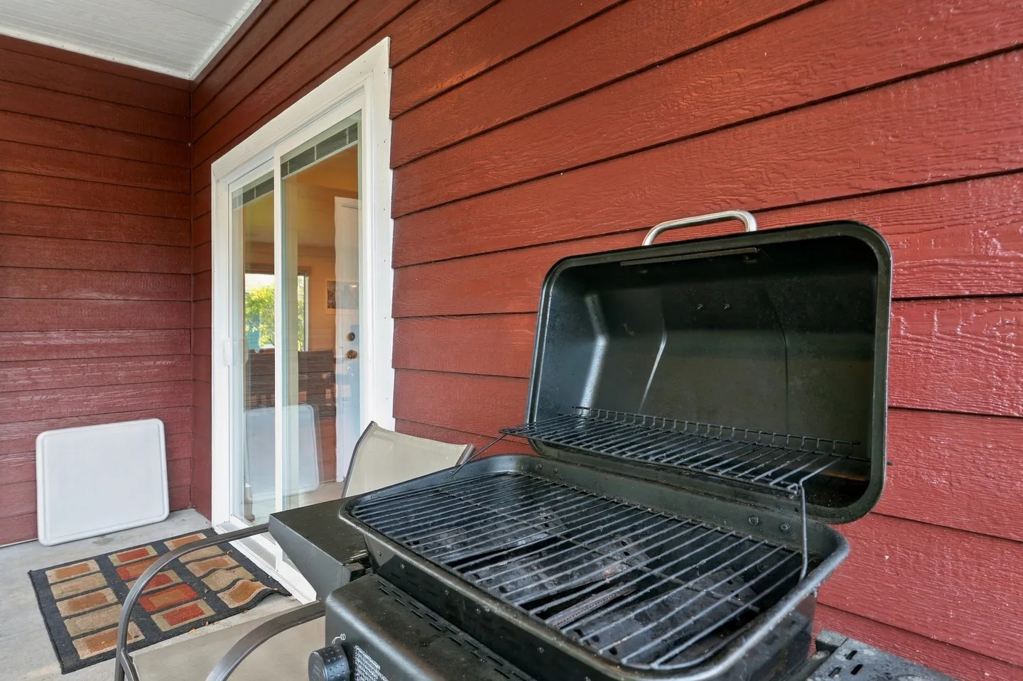 Open black barbecue grill on a concrete patio next to red siding and sliding glass doors.