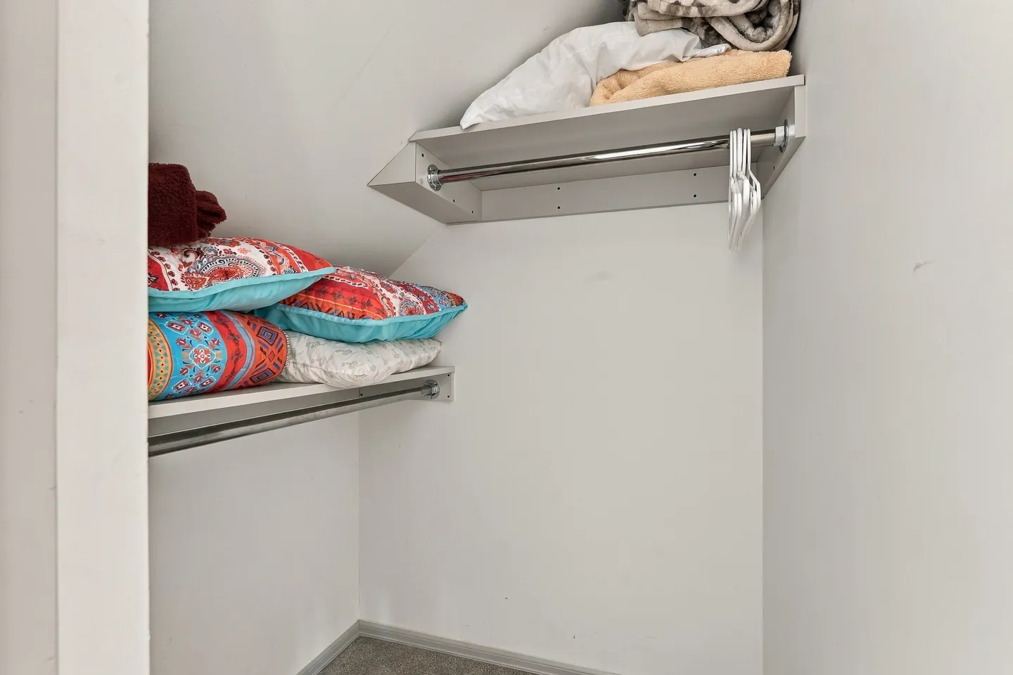 Under-stair closet with built-in shelves, clothes hanging rods, pillows, and extra linens.