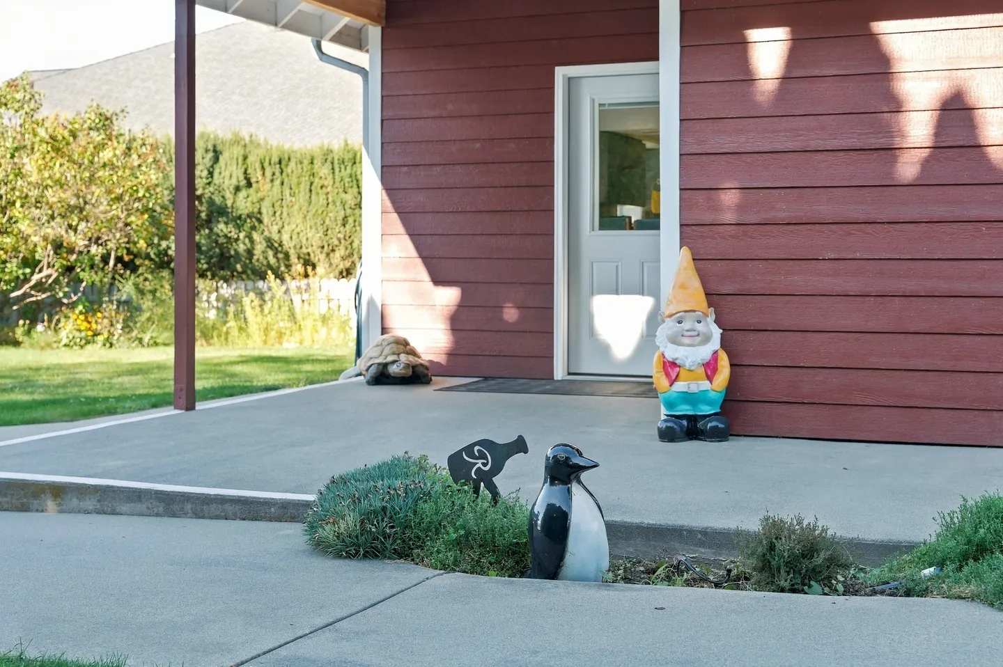 Exterior entryway with a concrete porch, red horizontal siding, a white door, and decorative garden figurines.