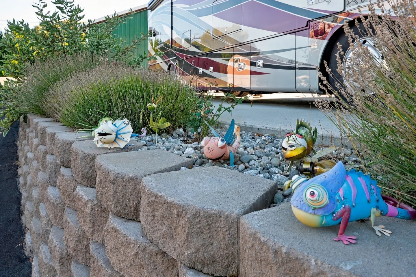 A low stone retaining wall decorated with colorful metal animal figurines next to a paved driveway with a parked motorhome.
