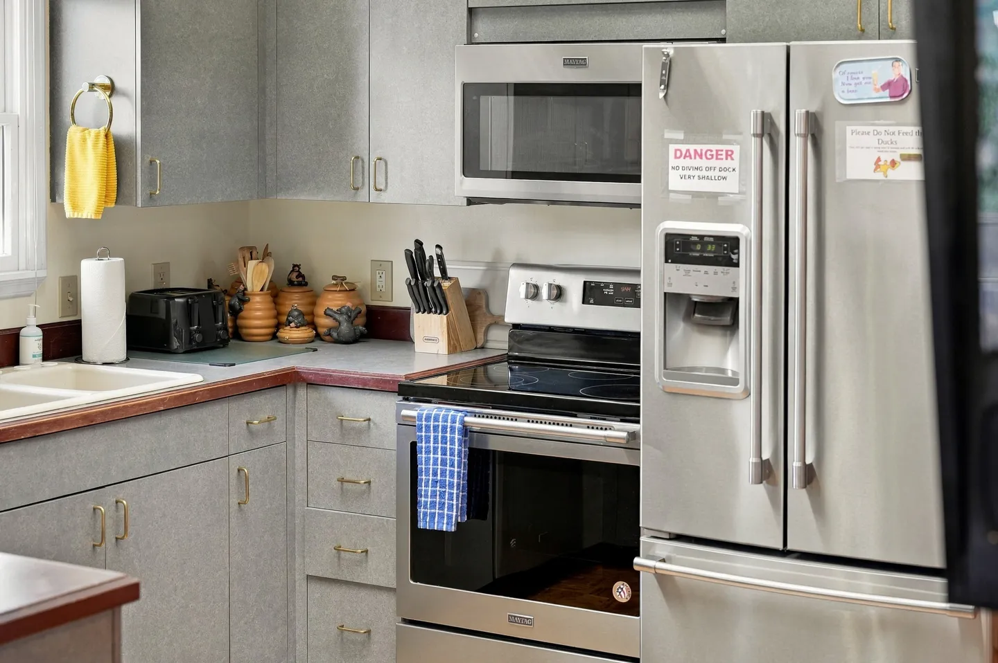 Kitchen corner showing grey cabinets, stainless steel appliances including a refrigerator, stove, and microwave, with countertop accessories.