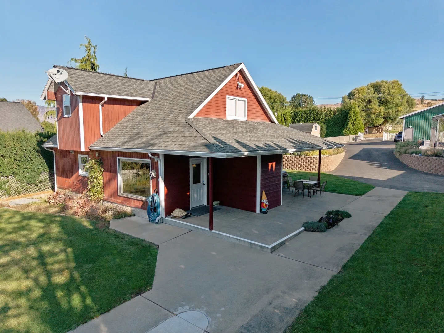 Exterior view of a red two-story house with a covered front patio, lawn, and concrete walkways under a clear blue sky.