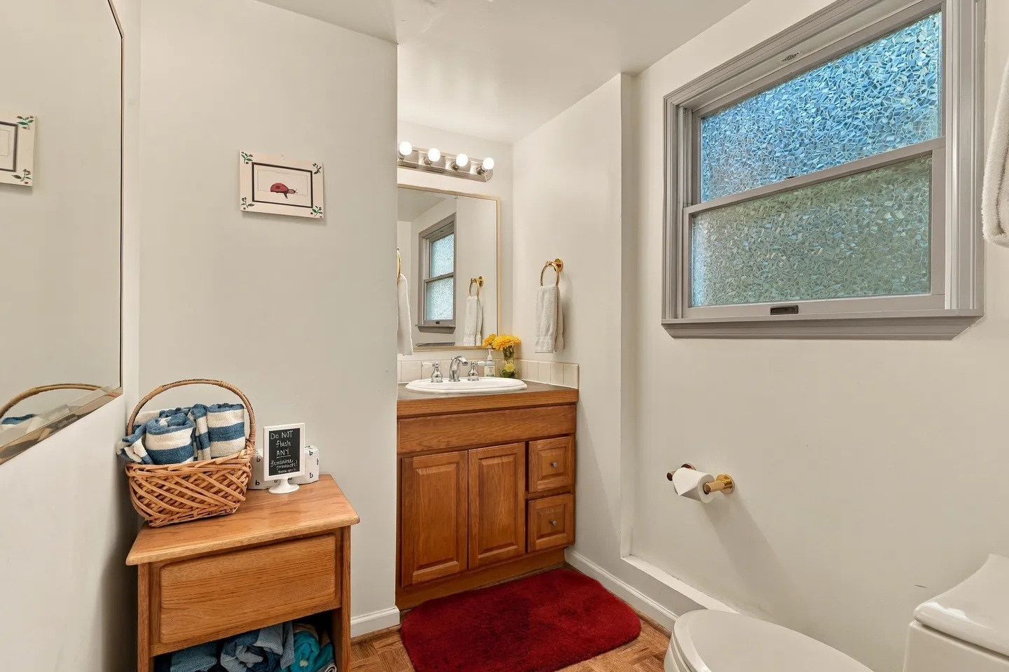 Bathroom featuring a wood vanity with a framed mirror, globe vanity lights, a textured glass window, and a red bath mat.