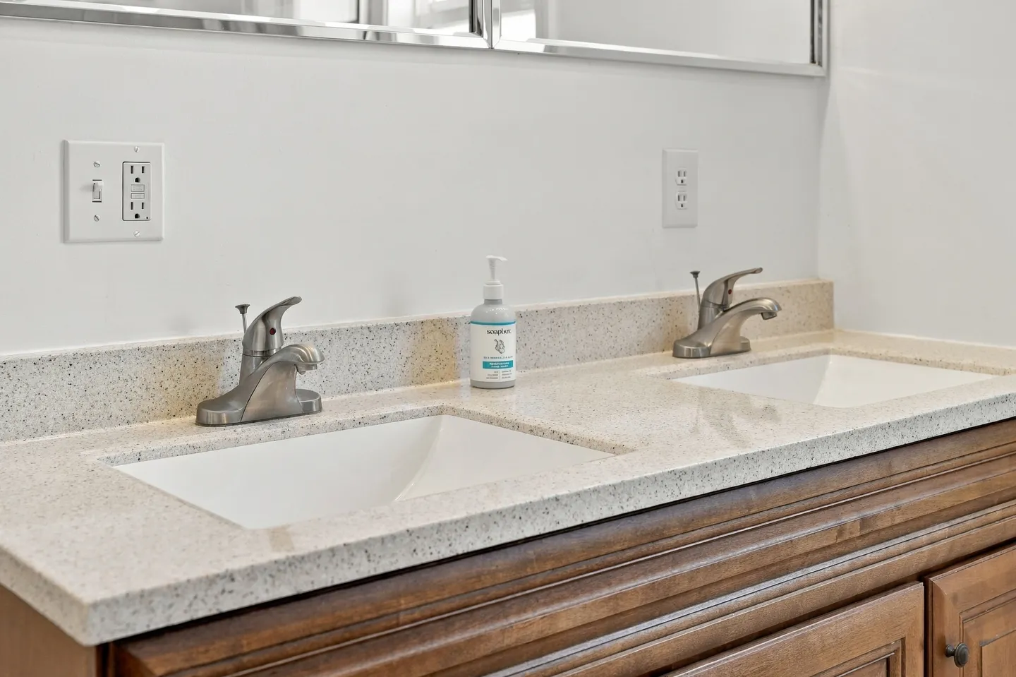 Close-up of a double bathroom vanity with speckled countertops, brushed nickel faucets, and rectangular undermount sinks.