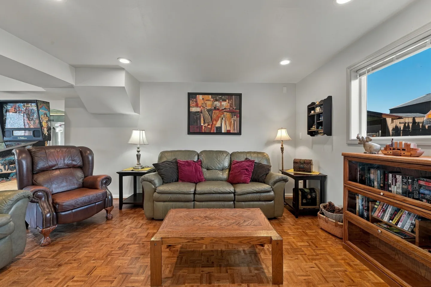 Living room with parquet flooring, a leather sofa, armchair, coffee table, and a pinball machine visible in the background.