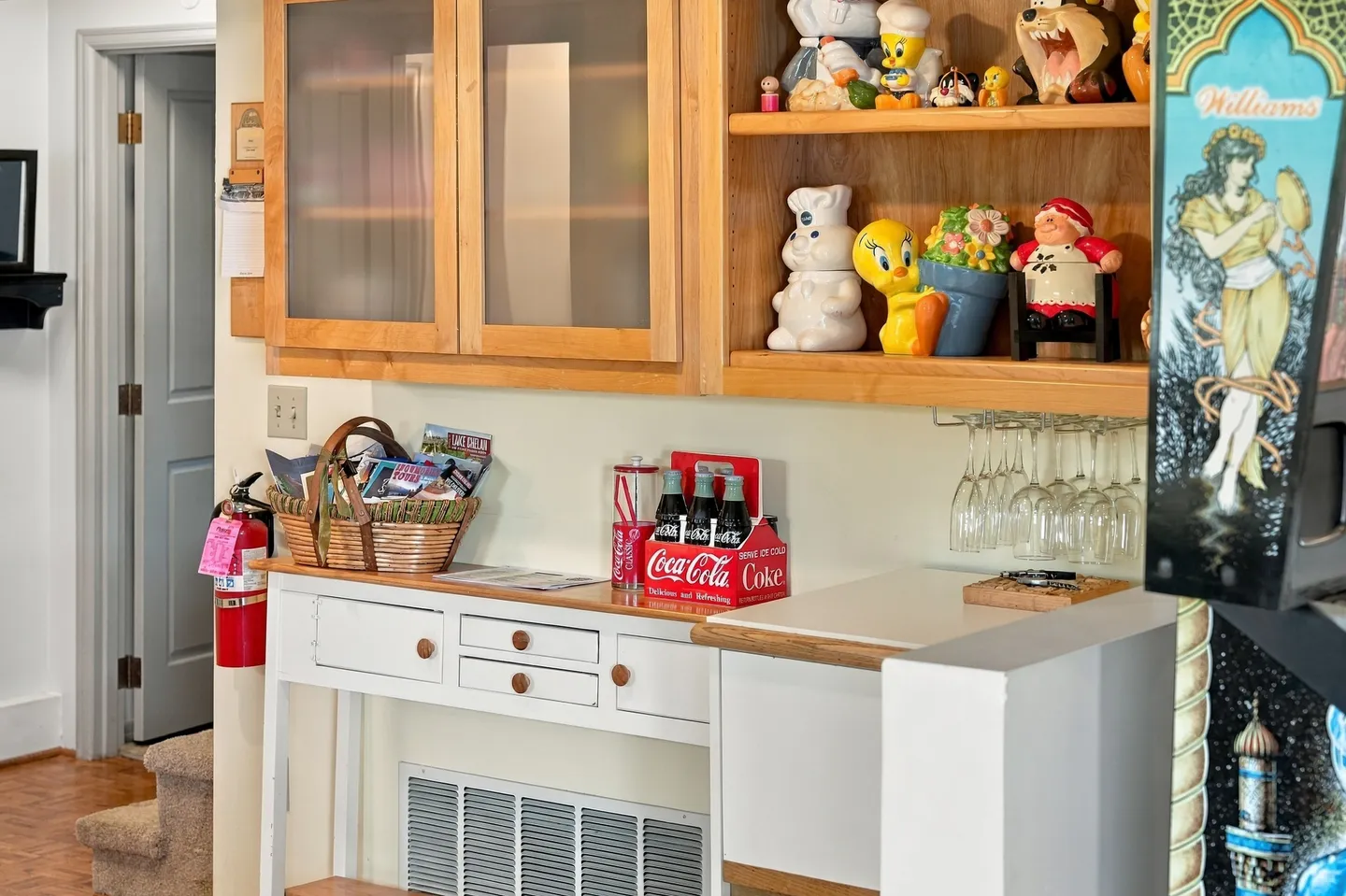 A built-in counter and upper cabinetry with figurines on display shelves, stemware rack, and a pinball machine edge visible nearby.