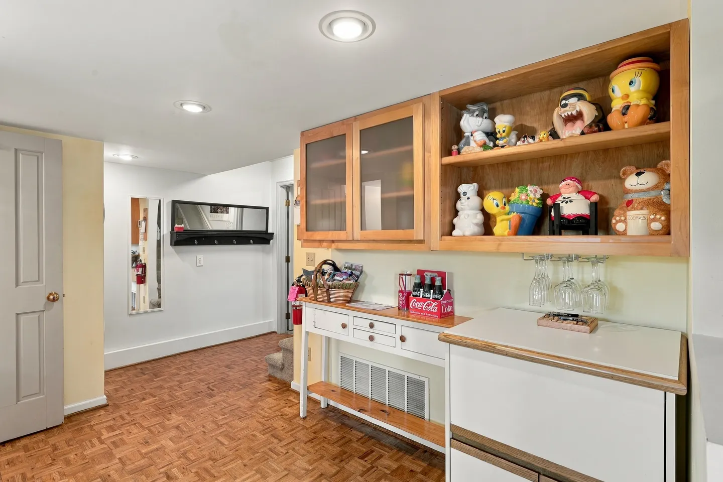 Indoor hallway and entryway area with parquet flooring, white console tables, and wooden display shelving with character figurines.