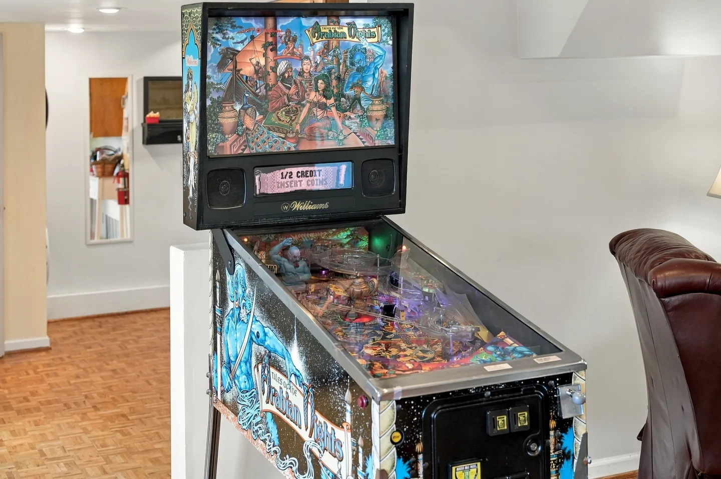 A Tales of the Arabian Nights Williams pinball machine set up indoors next to a leather recliner.
