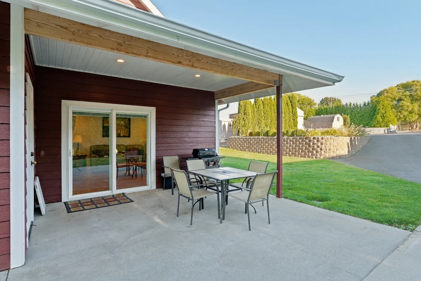 Covered concrete patio with an outdoor dining table, chairs, barbecue grill, and sliding glass door.