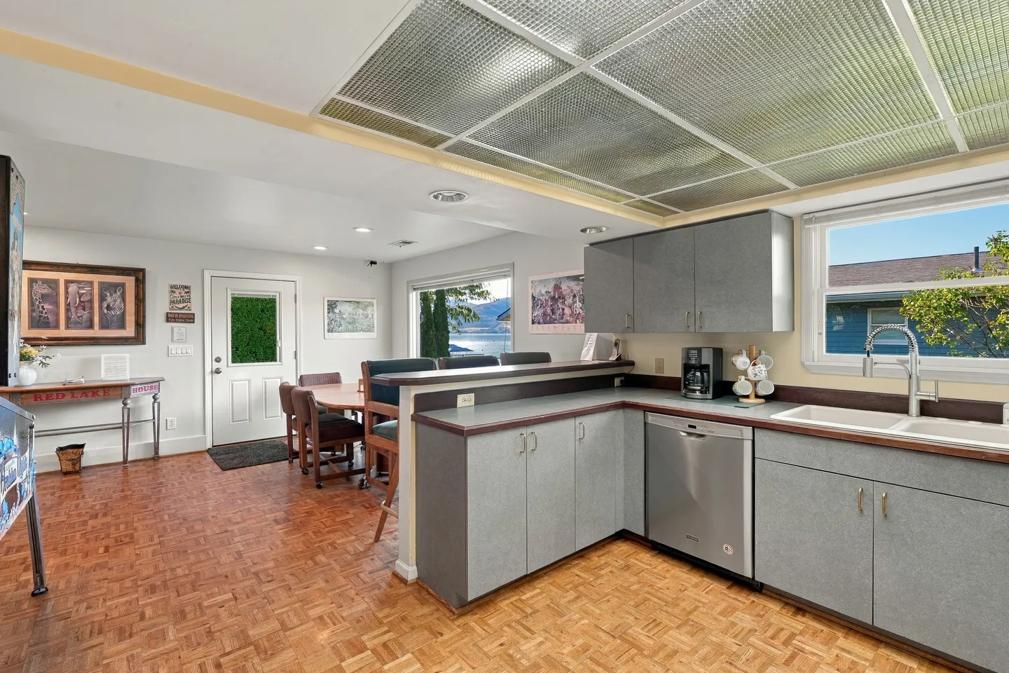 Kitchen with gray cabinetry, parquet flooring, and views looking toward a dining area and outdoor lake through the window.