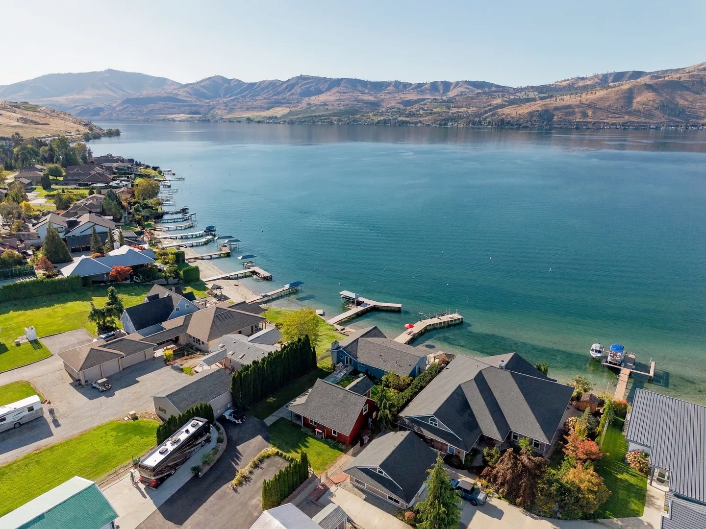 Aerial view of waterfront houses along a large blue lake with docks and mountains in the background