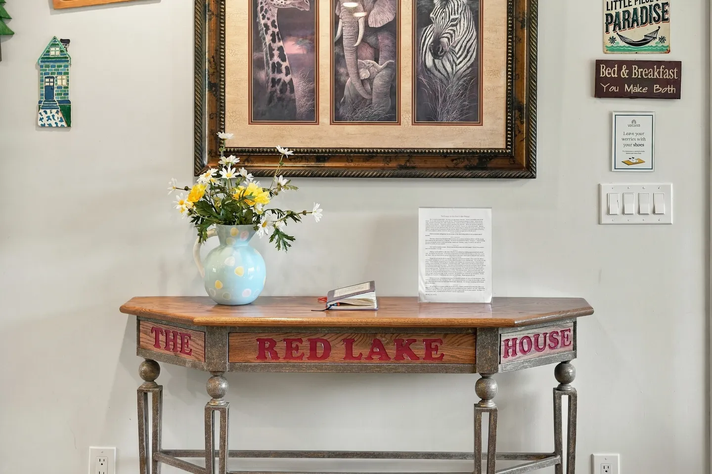 A wooden console table inscribed with 'THE RED LAKE HOUSE' against a white wall decorated with framed artwork and signs.
