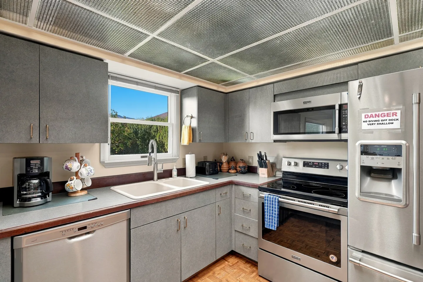 Kitchen with textured gray cabinets, stainless steel appliances, double sink, and a grid ceiling panel system.