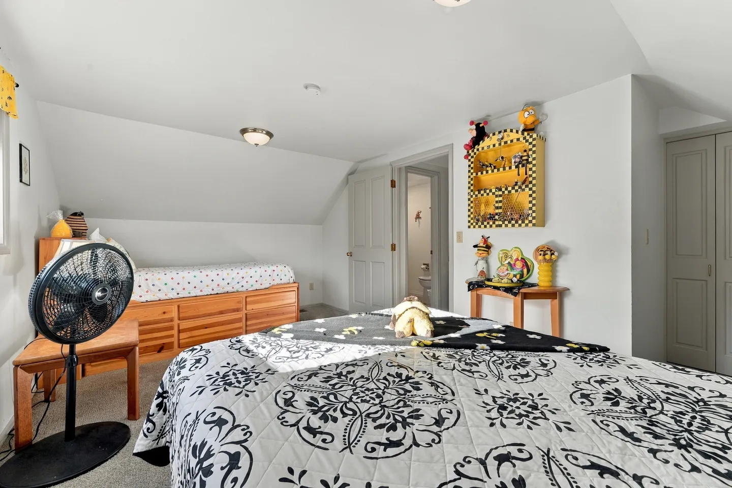 Bedroom with sloped ceiling, double bed in foreground, single captain's bed, small side tables, and an open doorway leading to a bathroom.