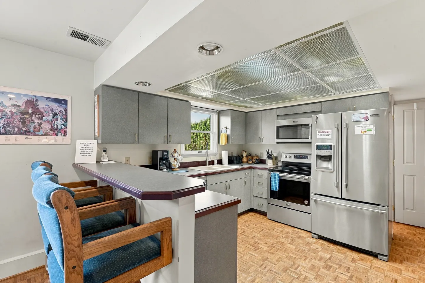 Kitchen with gray cabinetry, stainless steel appliances, parquet wood flooring, and a breakfast bar with upholstered chairs.