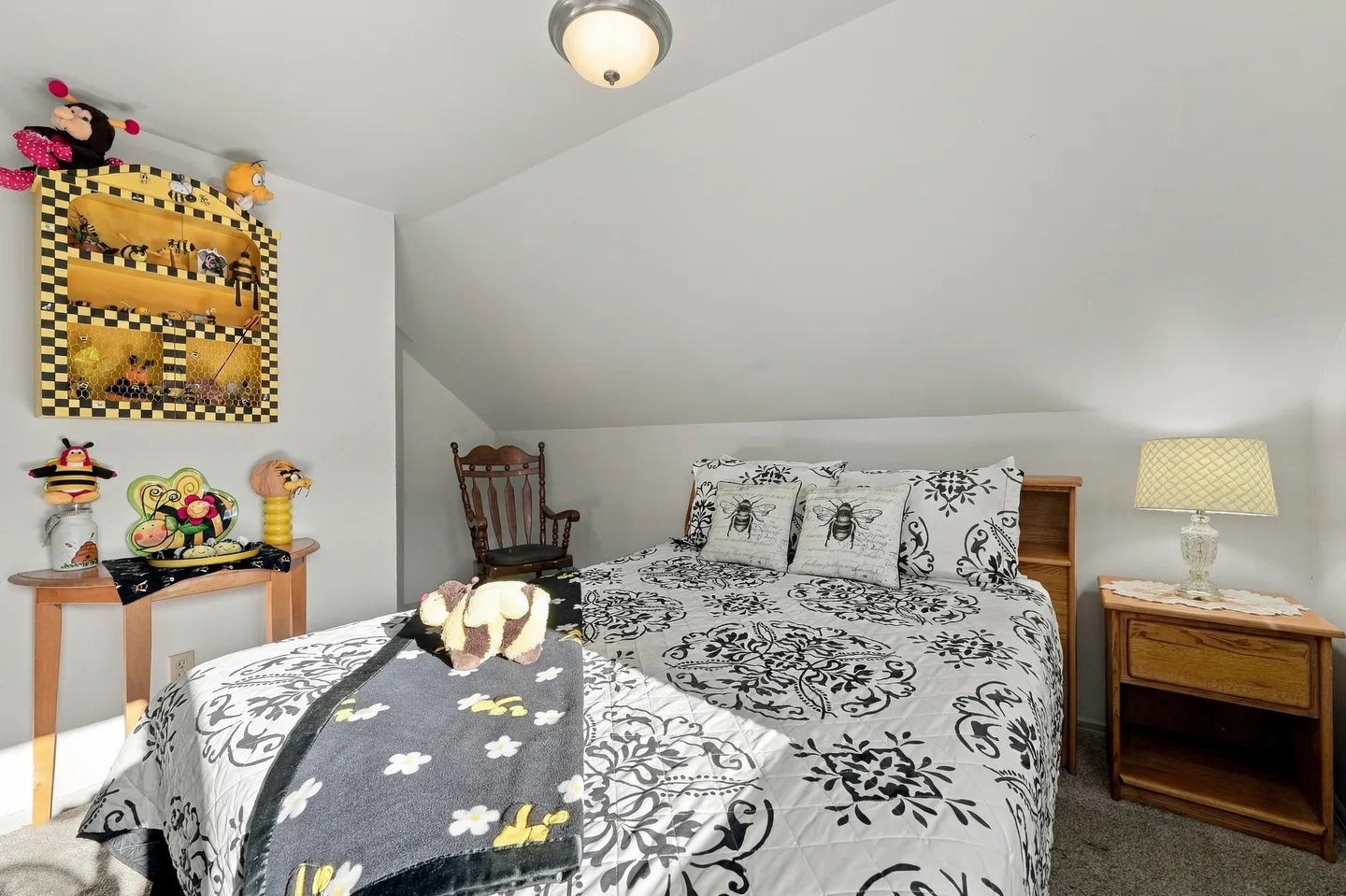 Bedroom with a sloped ceiling, a bed dressed in black and white patterned bedding, a nightstand, and bee-themed decorations.