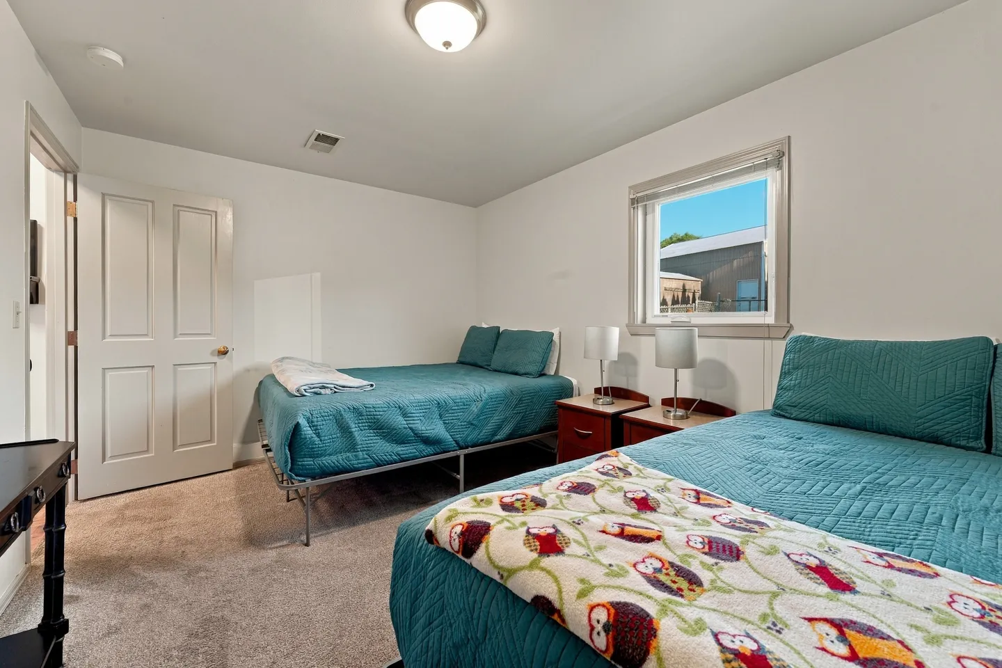 Bedroom with two beds made up in teal quilted bedding and a small nightstand under a window.