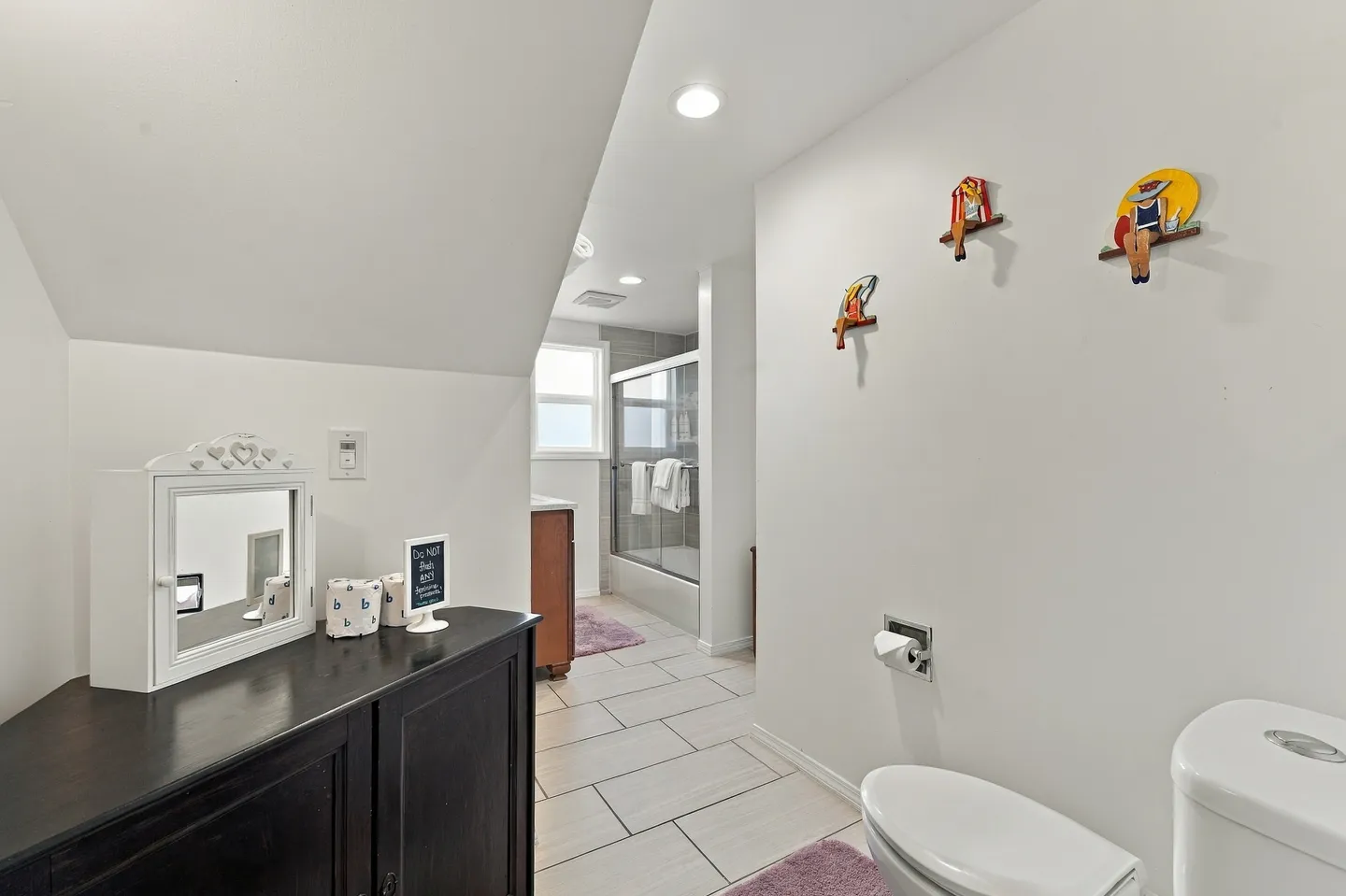 Bathroom with white walls, tiled floor, toilet, dark cabinet, and glass shower enclosure in the background