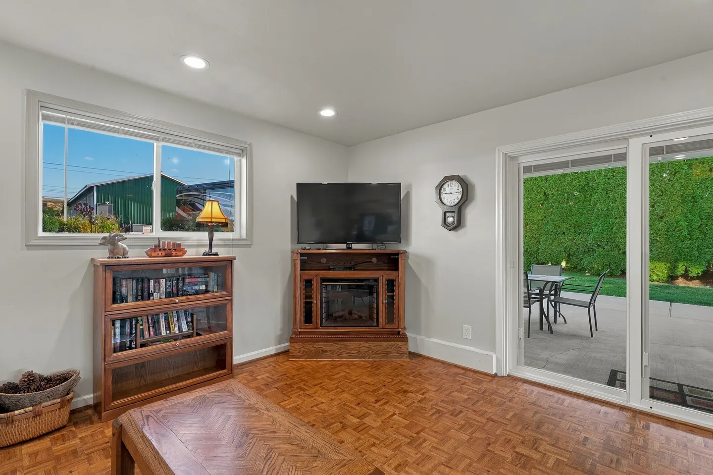 Living room corner with parquet wood flooring, a television on a wooden media stand, a low bookcase, and sliding glass doors to a patio.