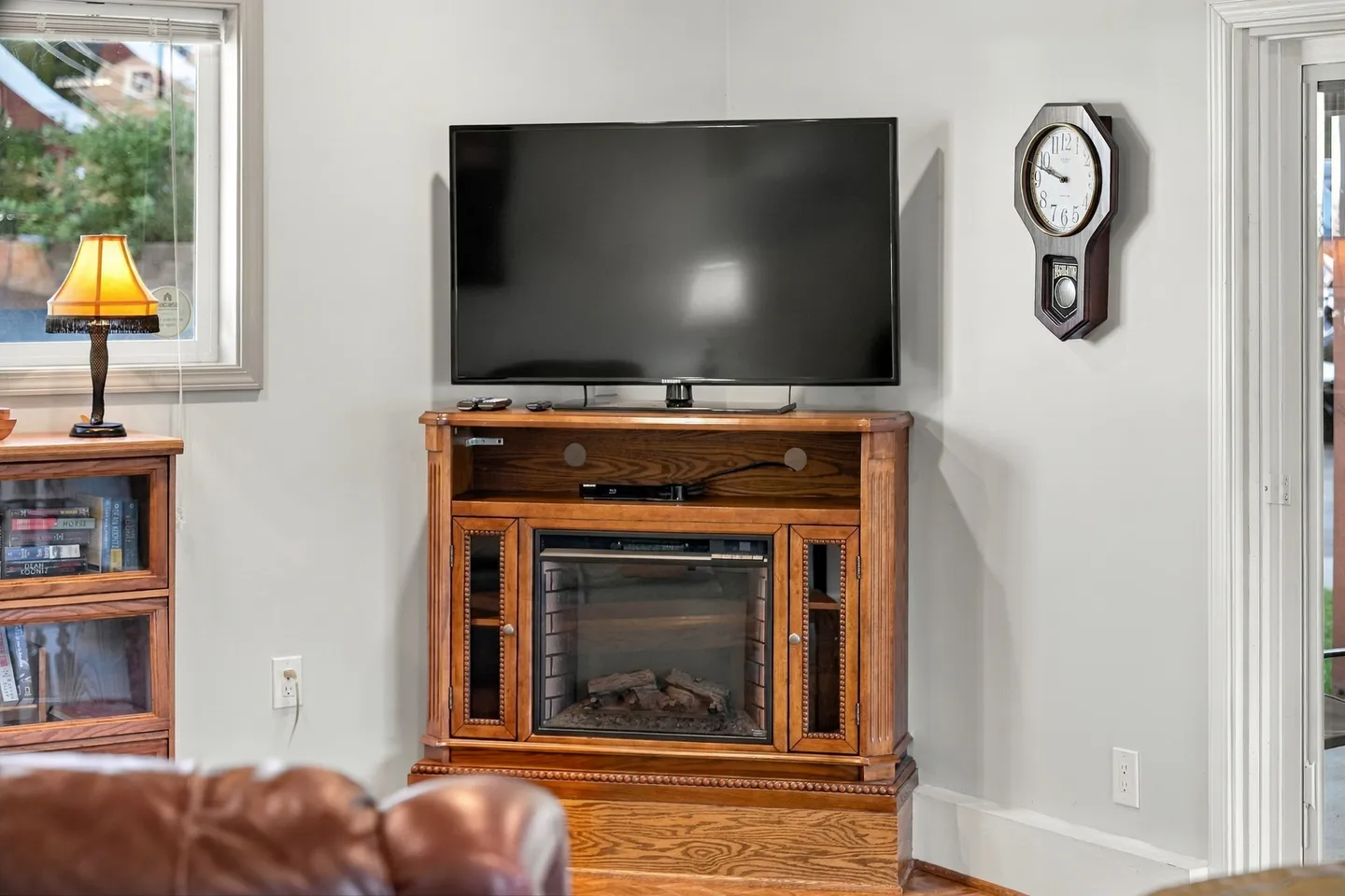 A corner wooden entertainment console with a flat-screen television and built-in electric fireplace next to a wall clock.