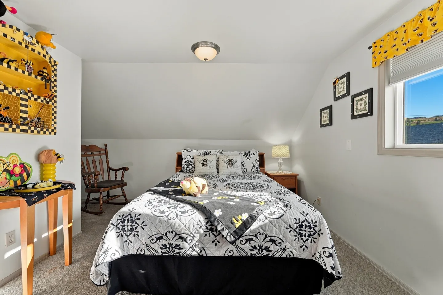 Bedroom with a patterned bedspread, bee-themed decor, sloped ceiling, and carpeted floor.