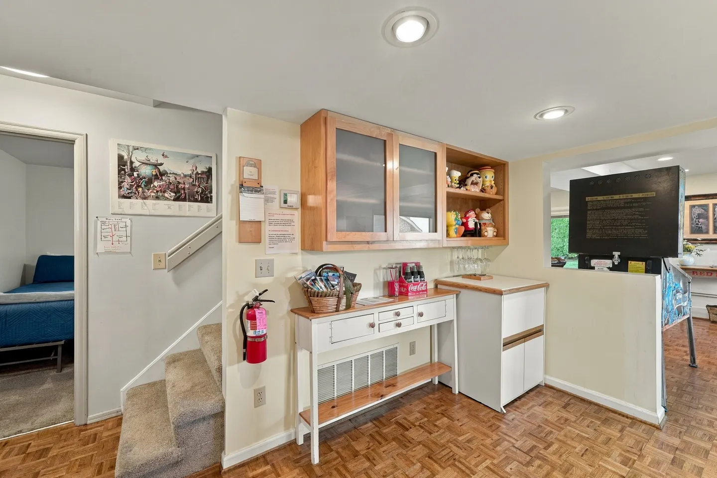 Lower-level interior hallway with parquet flooring, storage cabinets, stairs, and a doorway to a bedroom.