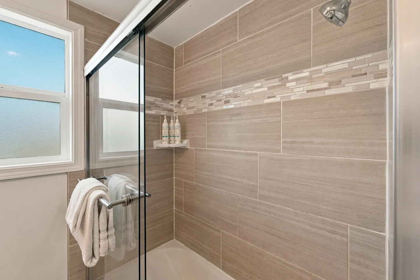 Bathroom shower and bathtub combo with beige tiled walls, sliding glass doors, and a frosted window.