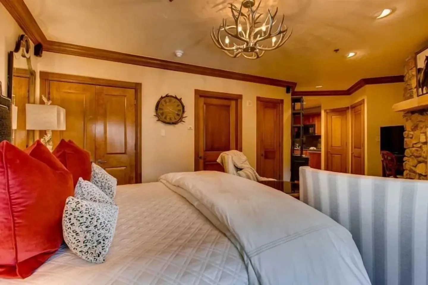 Bedroom featuring a bed with bright red accent pillows, an antler chandelier overhead, and warm wood trim and doors.