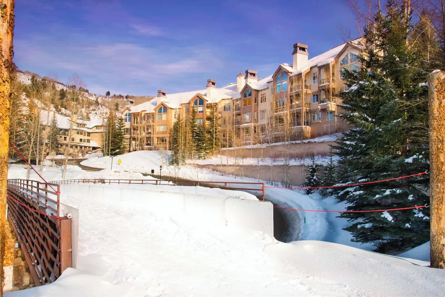 Exterior view of a multi-story mountain lodge building during winter, surrounded by snow and evergreens.