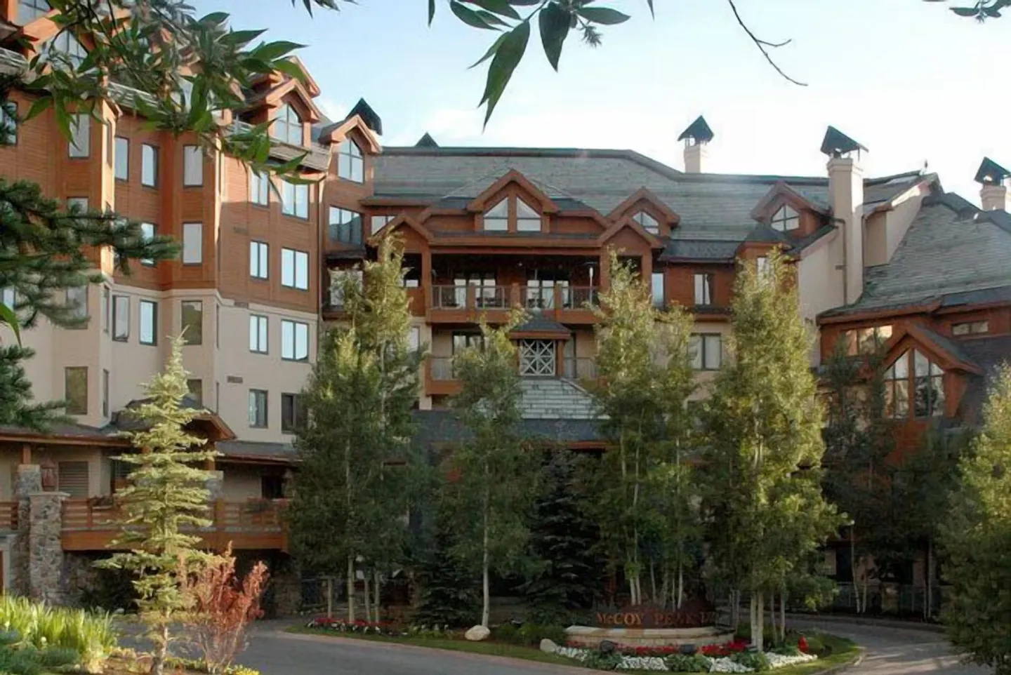 Exterior view of McCoy Peak lodge building with timber siding, multiple balconies, gabled roofs, and evergreen and deciduous trees in front.