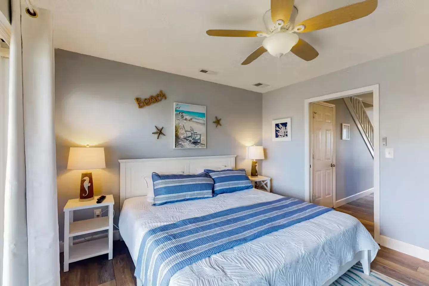 Bedroom with a white headboard, blue-and-white bedding, bedside tables with lamps, and a ceiling fan.