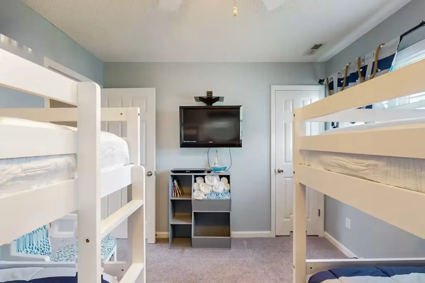 Bedroom with two sets of white wooden bunk beds flanking a wall-mounted TV and shelving unit.