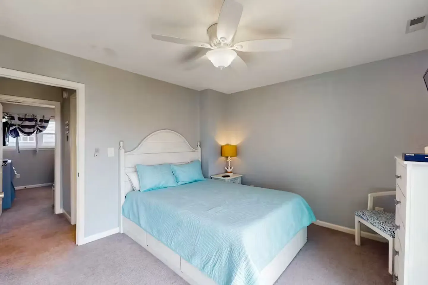 Bedroom with light blue bedding, white headboard, ceiling fan, and carpeted floor.