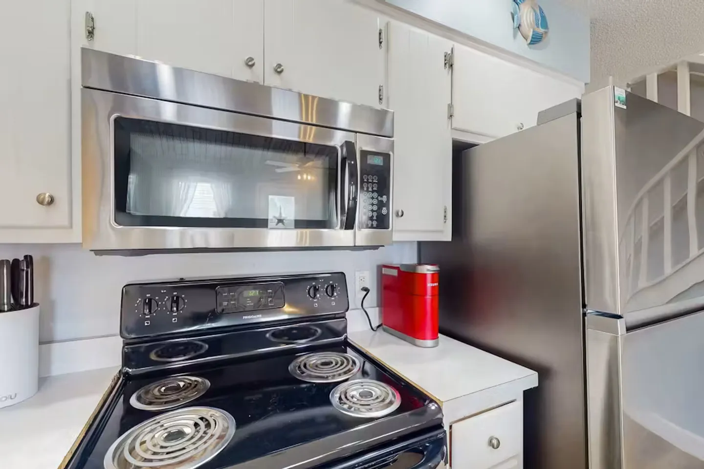 Kitchen area showing a black electric stove, an over-the-range stainless steel microwave, white cabinets, and a stainless steel refrigerator.